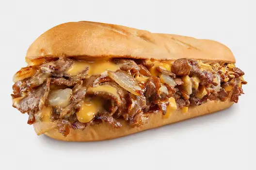 Chicken Philly Cheesesteak from Charleys Rosedale Cheesesteaks against a white background. This is make with grilled chicken, peppers, and onions with provolone on a toasted roll. This is served with lettuce, tomato, mayo, and pickle. Philly chicken cheesesteak near me.